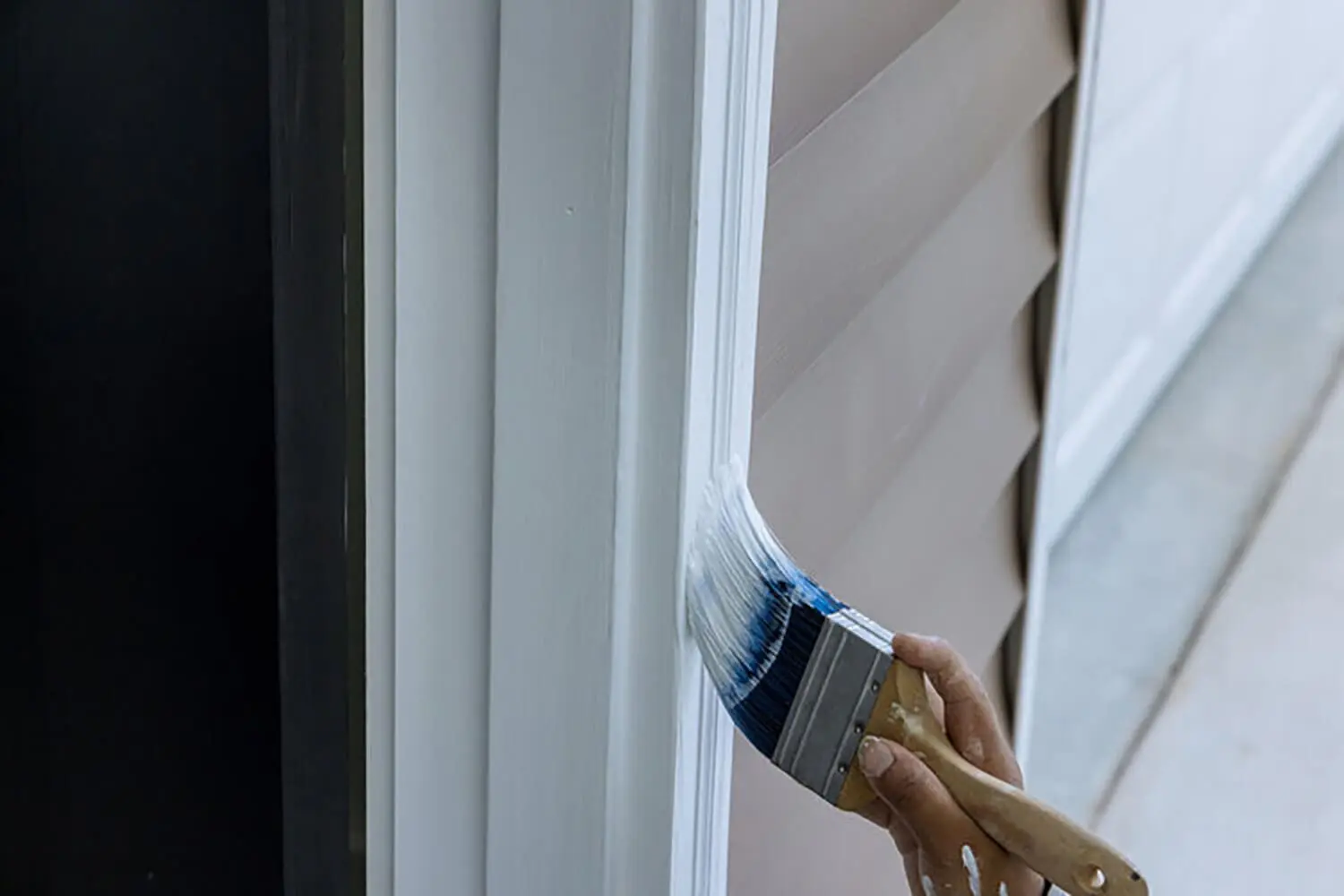 Painter brushing dark blue paint onto exterior window trim on a home with lap siding.