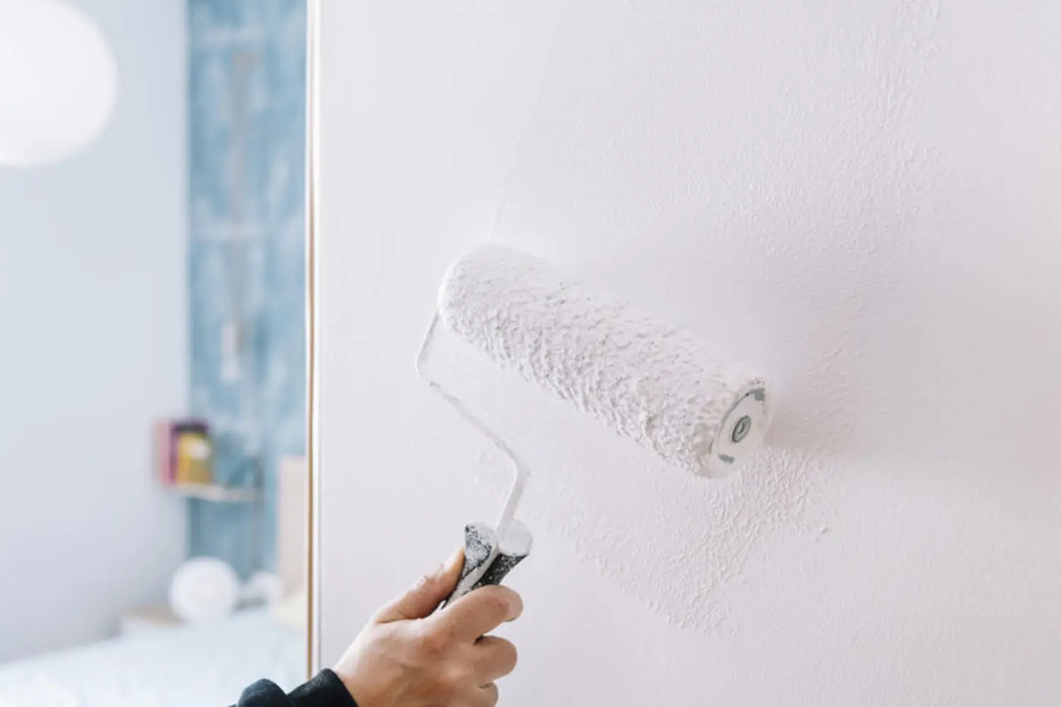 Painter rolling white paint onto an interior wall with blue tile visible in the background.