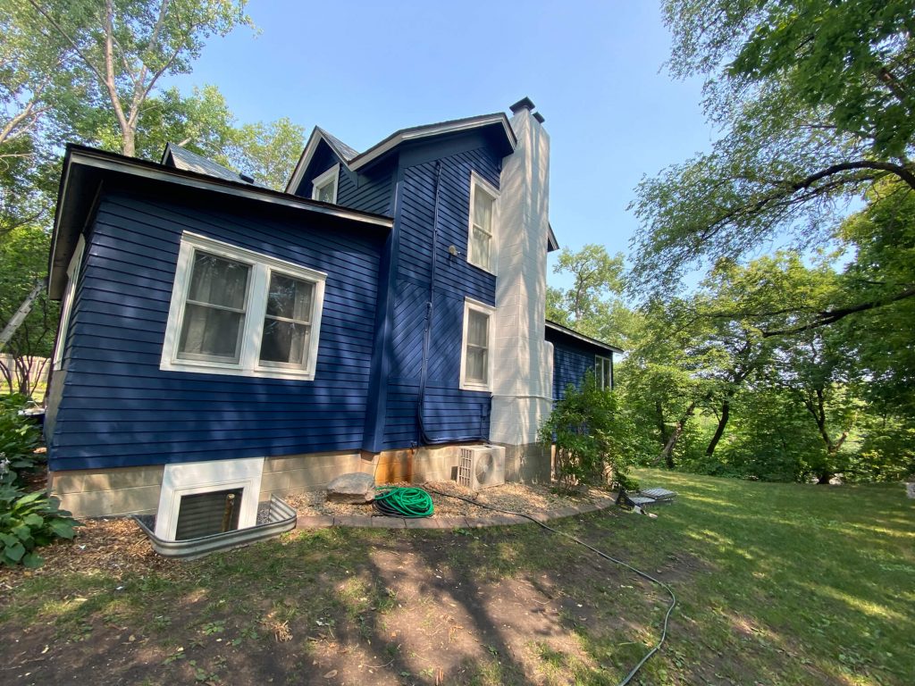 Finished exterior house painting by Chrave Davis Painting, showcasing a striking dark blue siding and white trim in a wooded setting.